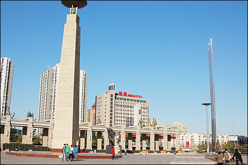 베이징 왕징에 세워진 상징탑. 한글을 포함한 다양한 언어로 '더 높게'라는 글자가 쓰여 있다. 멀리 보이는 건물(broadtec)에 재중한국인회가 입주해 있다. 